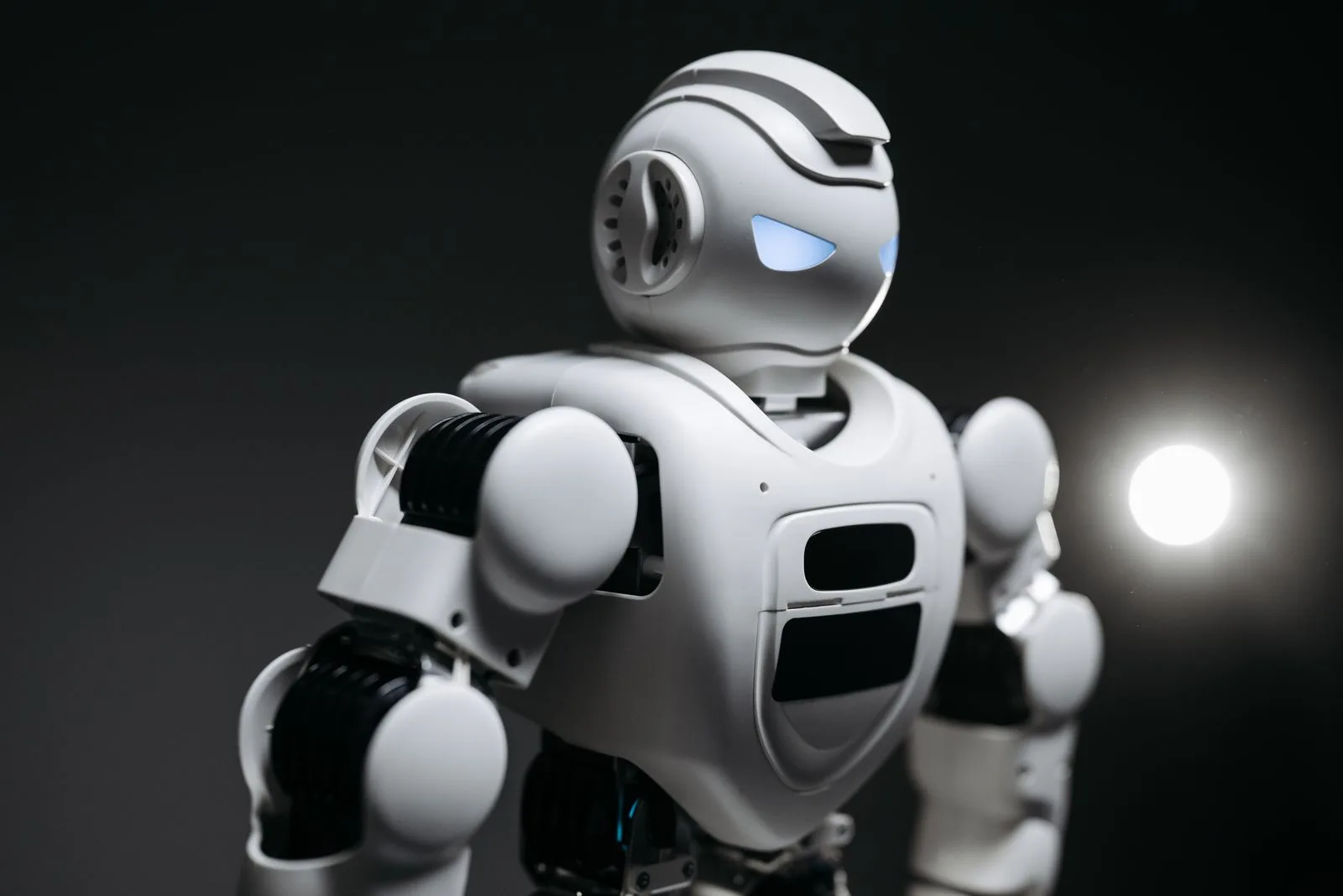 White robot with glowing eyes in dramatic dark studio lighting, representing always-on AI agents