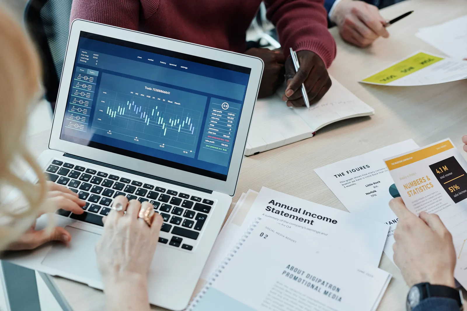 Finance professionals around a table reviewing an annual income statement and reports beside a laptop showing financial charts