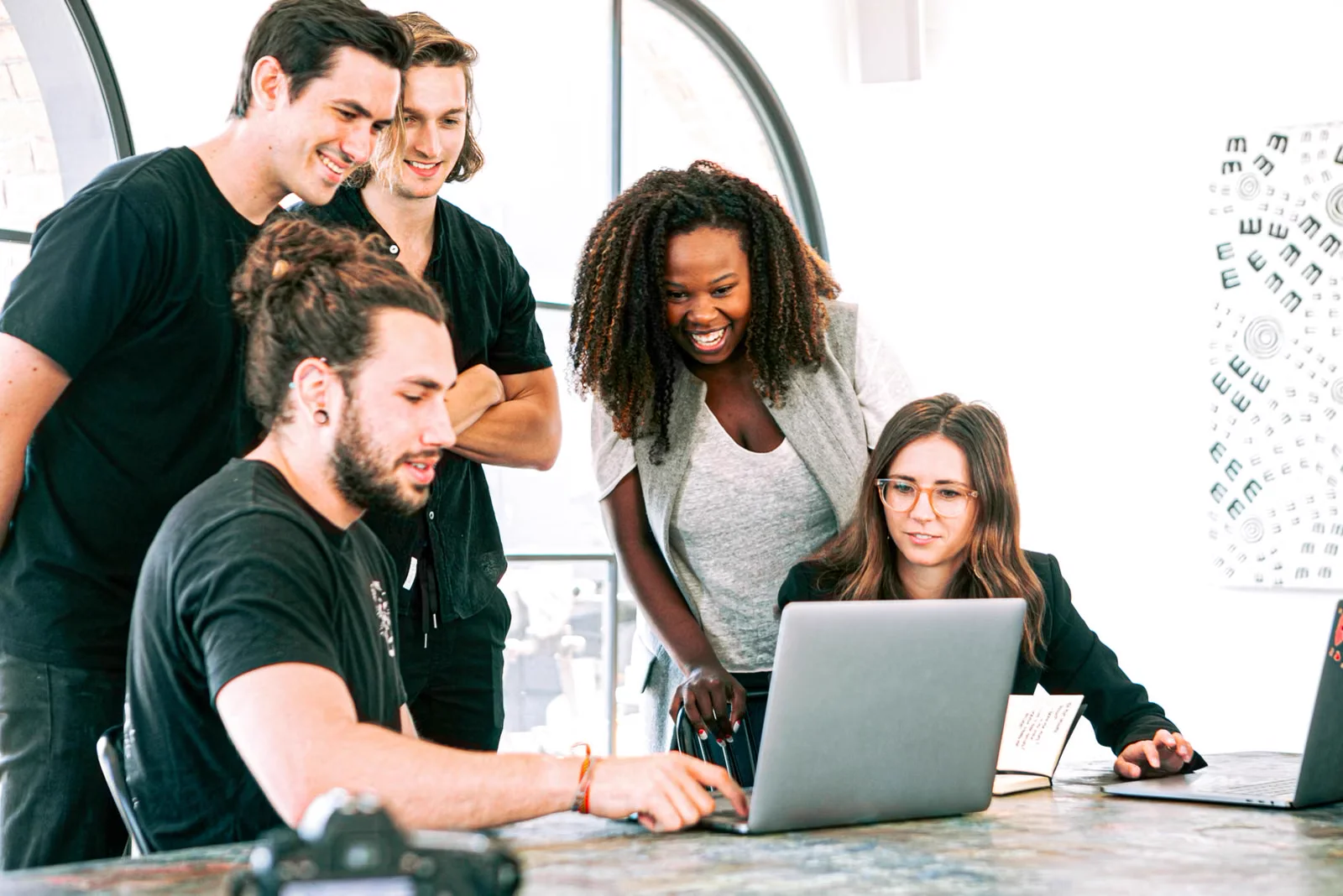 Smiling teammates collaborating closely around a laptop in a bright office