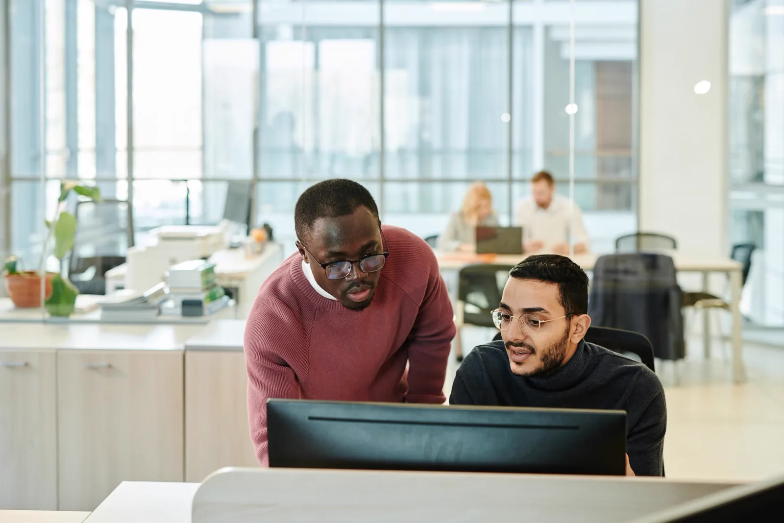 Senior colleague guiding a teammate over a computer screen